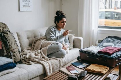 Sick woman on her couch, worried after checking her temperature with packed bags around her